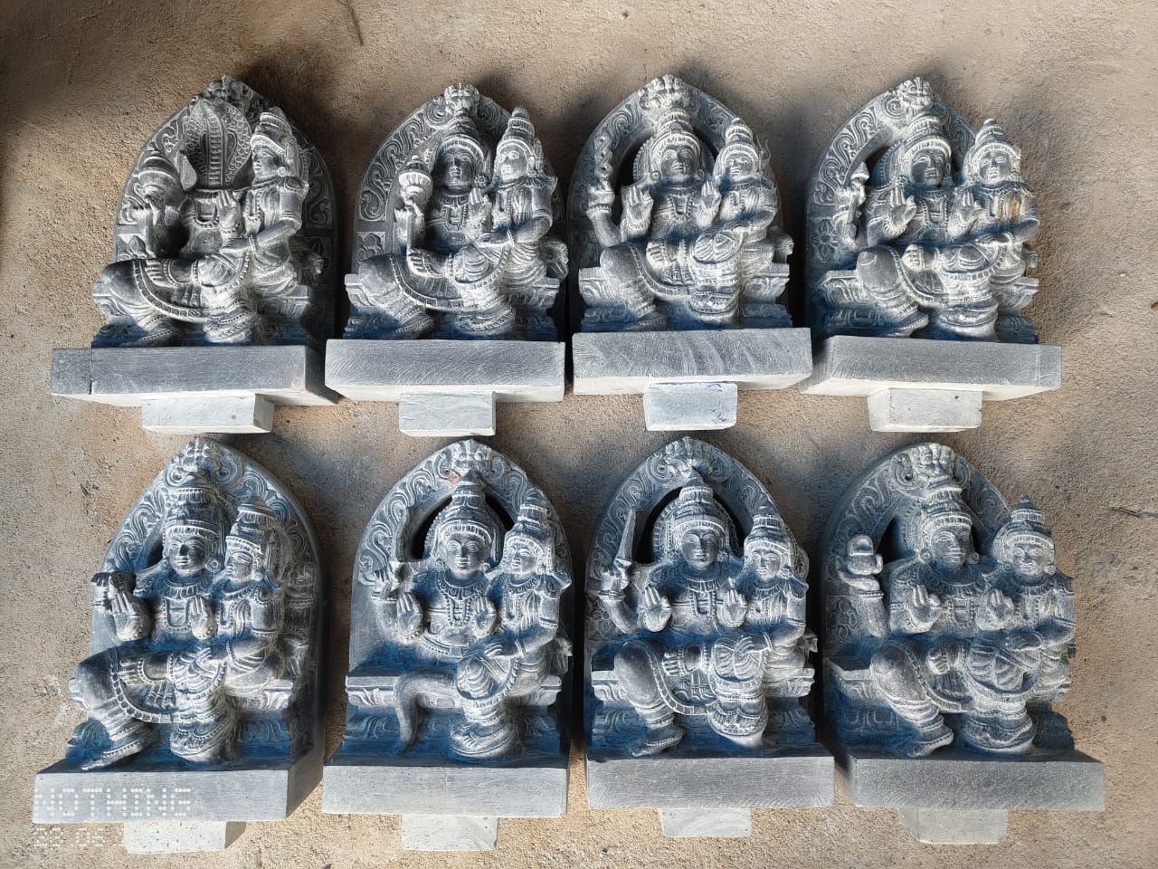 A set of eight carved deity panels in grey granite, each showing a different deity in arched niche