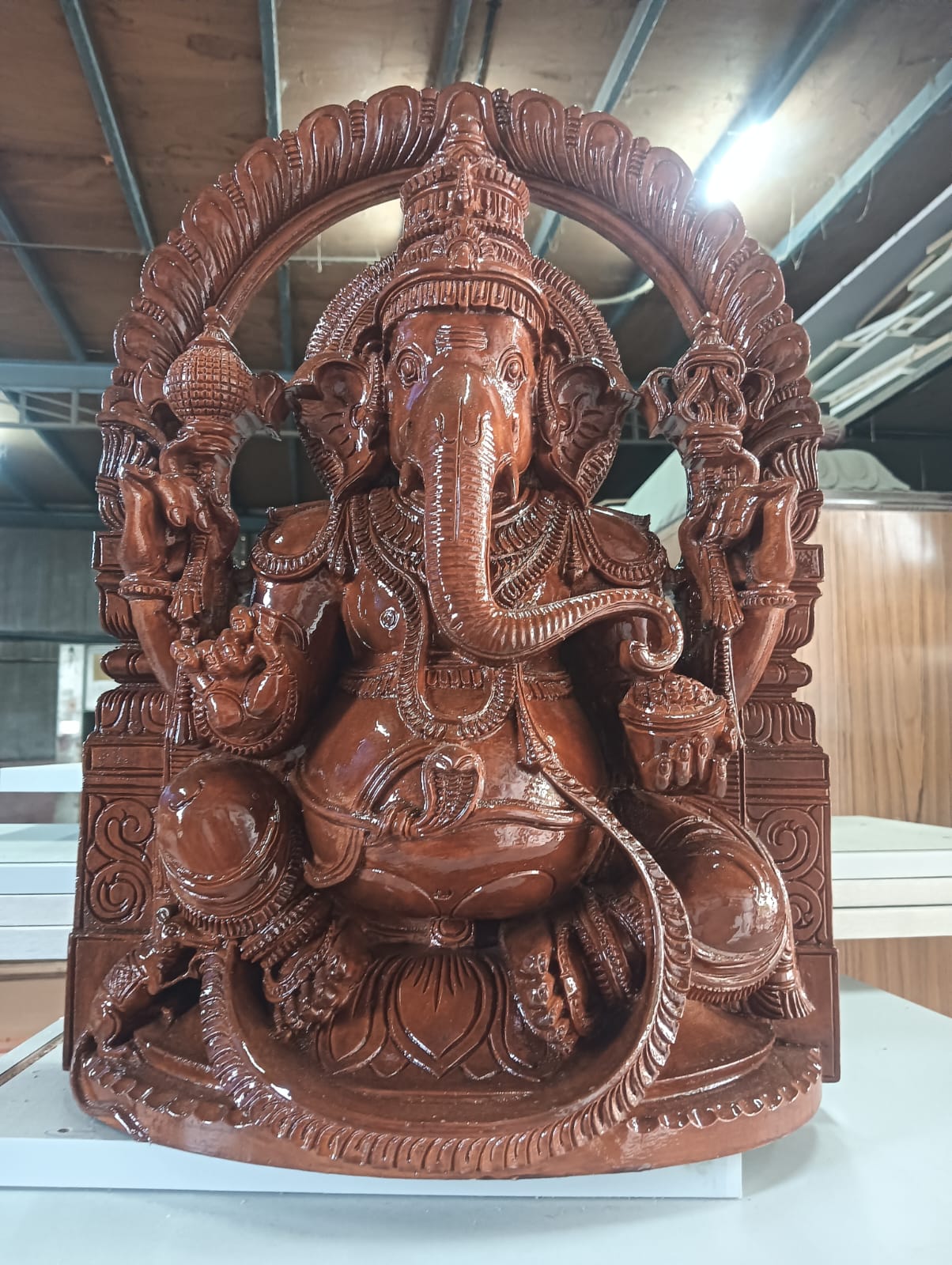 Intricately carved seated Ganesha in reddish-brown sandstone with ornate prabhamandala arch